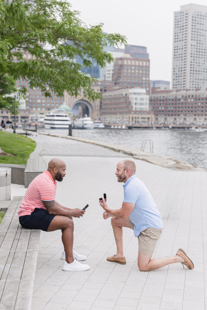 A man proposing to his fiancee with the Boston skyline in the background.