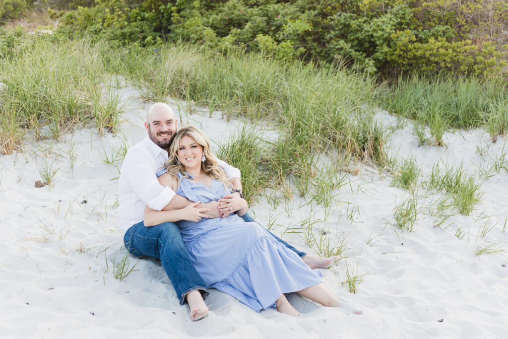 engaged couple cuddles on the sand dunes