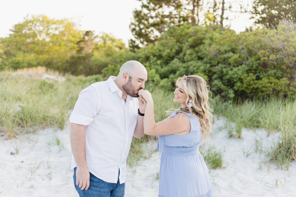 man kisses his fiancee's hand at wingaersheek beach
